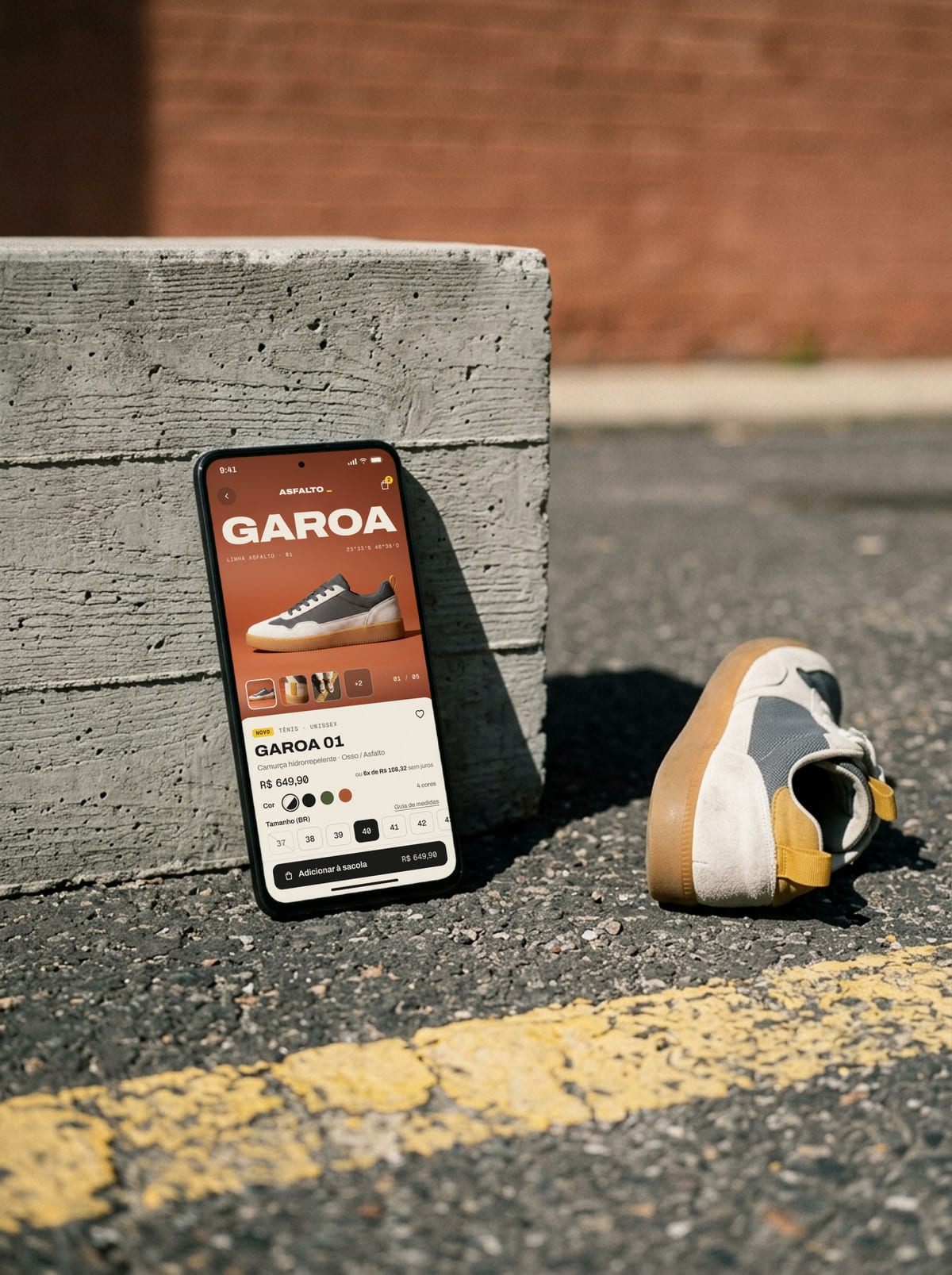 Celular apoiado no concreto mostrando a página do tênis GAROA 01 na loja fictícia ASFALTO, com tamanhos e o botão de comprar.