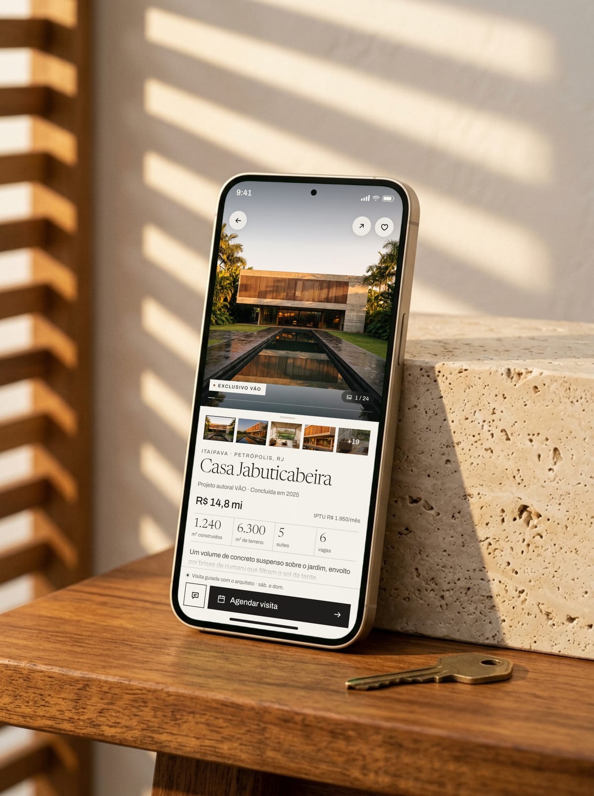Celular apoiado num bloco de travertino mostrando a página de uma casa no site do estúdio fictício VÃO, com o botão de agendar visita.